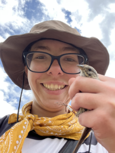 College holding a bird in her hand and smiling.