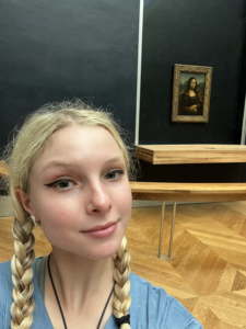 Mary is standing in front of the famous painting of Mona Lisa.